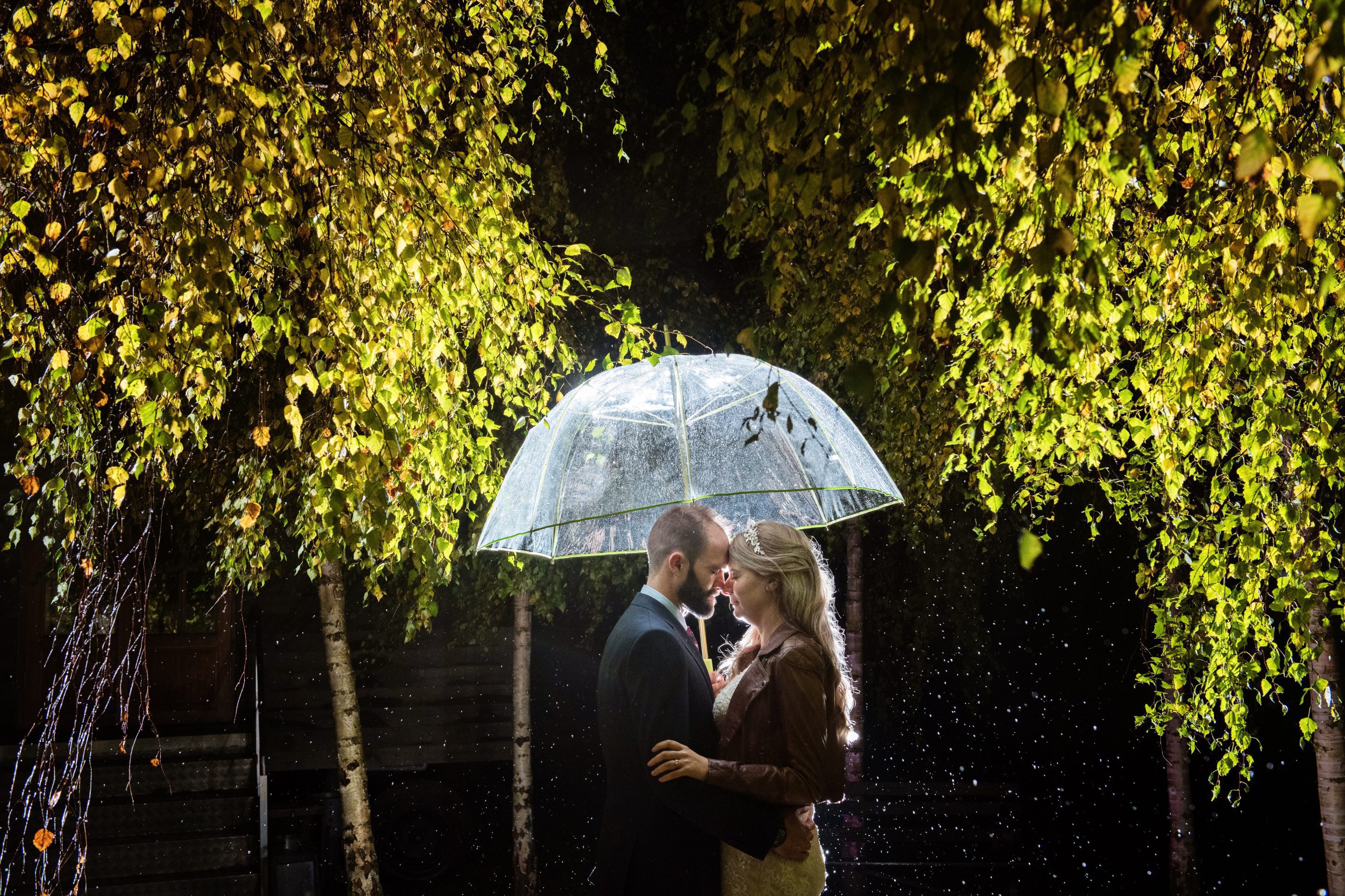 Bride and groom kiss in the rain under a umbrella.